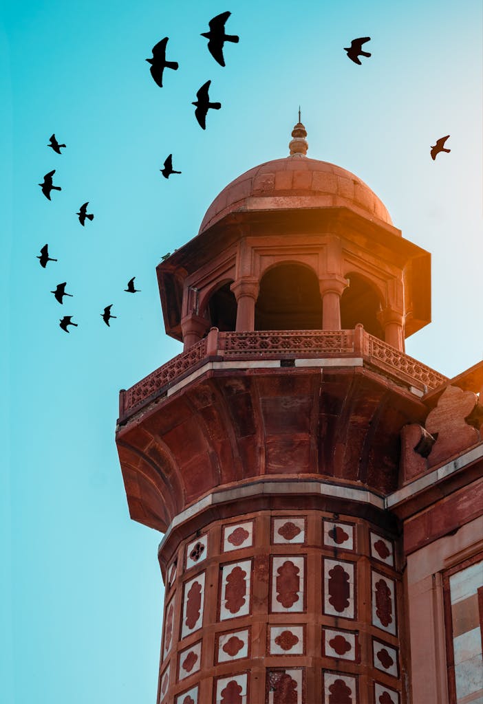 A stunning view of a historical minaret in New Delhi with birds in flight against a clear blue sky.